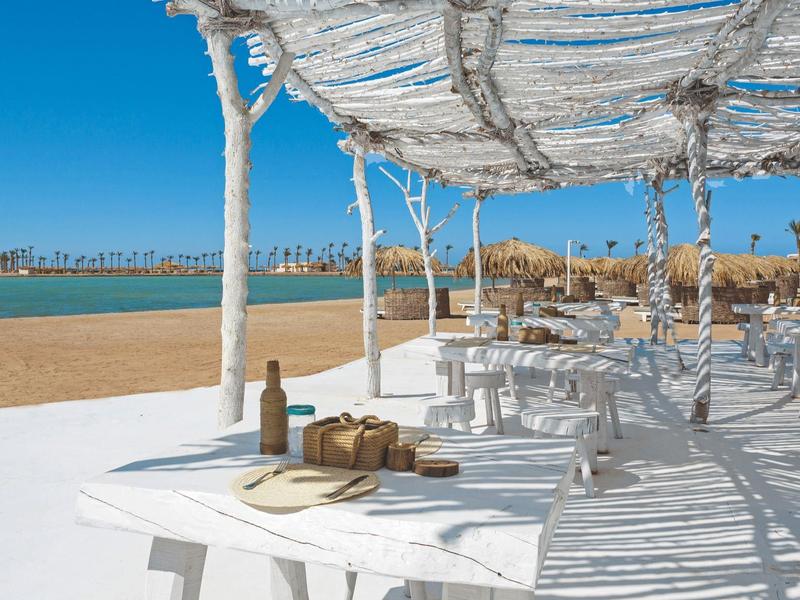 Sonniger Terrassenbereich mit weißen Tischen und Meerblick an einem Strandhotel.