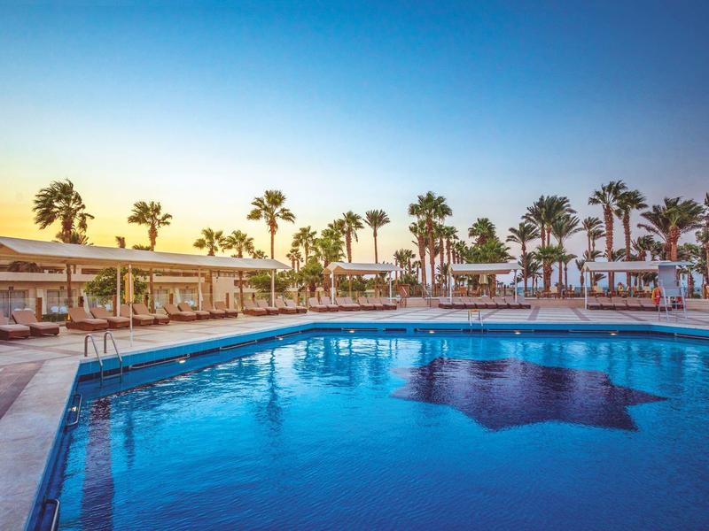 Großer Pool mit Palmen und Sonnenuntergang am Hotelresort.