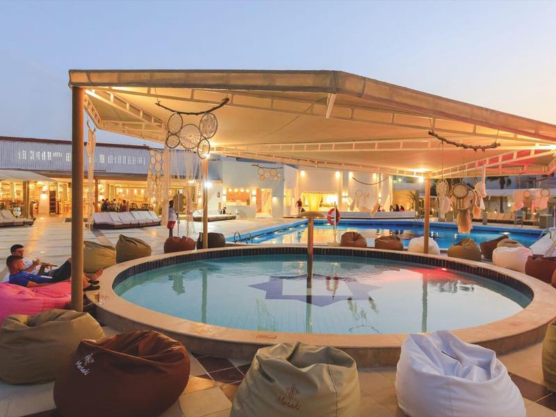 Runder Pool mit Sitzsäcken unter überdachtem Außenbereich in entspannter Hotelumgebung.