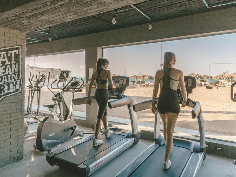 Zwei Frauen trainieren auf Laufbändern in einem Fitnessraum mit großer Fensterfront und Außenblick.