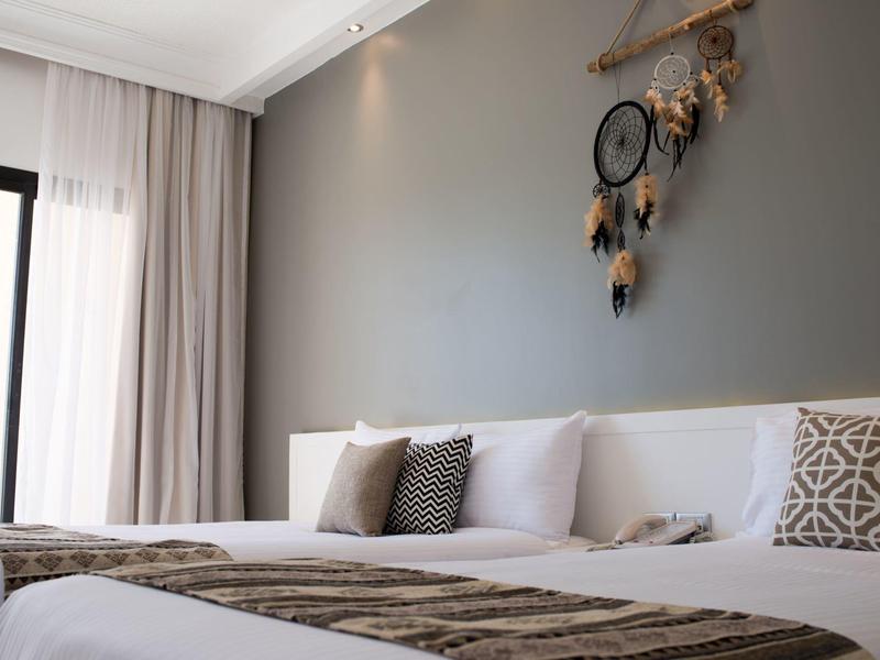 Modernes Hotelzimmer mit zwei Betten, Kissen und dekorativem Traumfänger an grauer Wand.