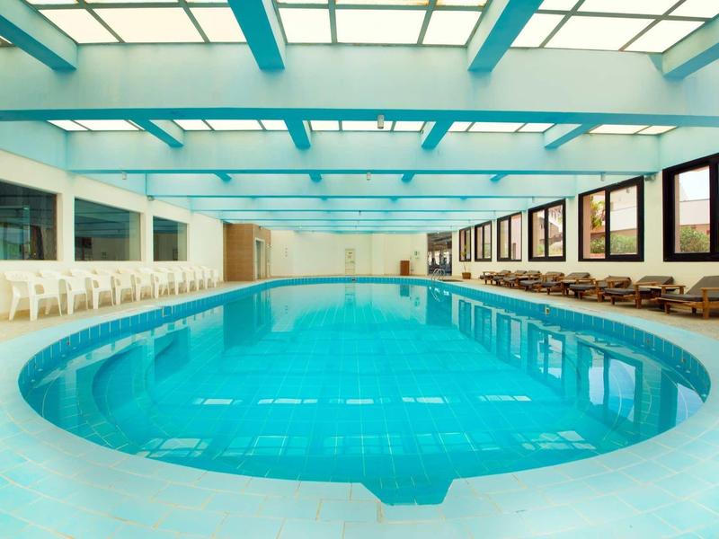 Piscine intérieure moderne avec transats et grandes fenêtres illuminées.