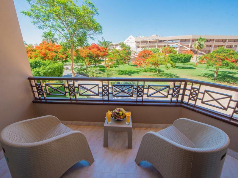 Balcon d'hôtel avec deux fauteuils et table, vue sur jardin fleuri et bâtiment.