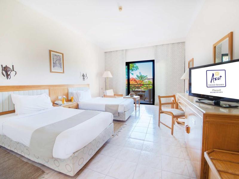 Chambre d'hôtel lumineuse avec deux lits, télévision et balcon avec vue sur la mer.