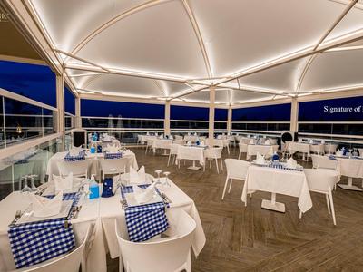 Elegantes überdachtes Restaurant mit weißen Tischen und blau-weiß karierten Servietten bei Nacht.