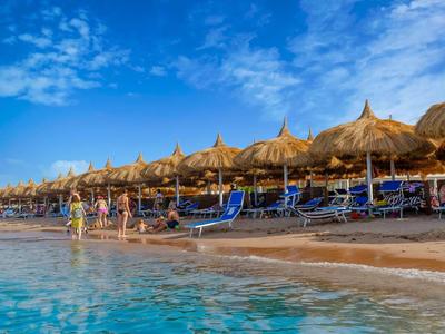 Strand mit Strohdach-Sonnenschirmen und Liegestühlen am klaren blauen Wasser unter blauem Himmel.