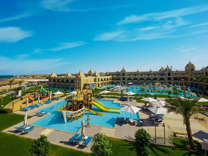 Grand complexe hôtelier avec plusieurs piscines, toboggans aquatiques et transats sous un ciel bleu.