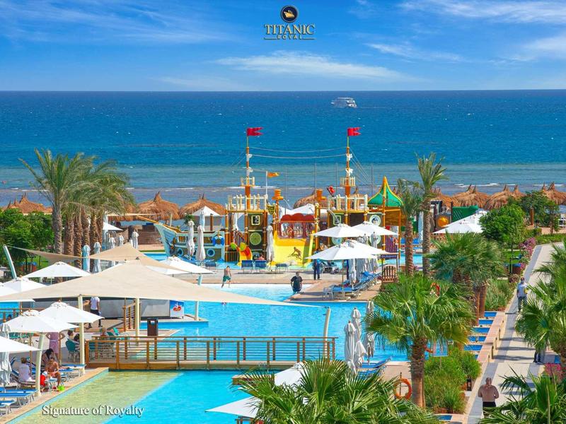 Vue sur une piscine d'hôtel avec parc aquatique et mer en arrière-plan sous un ciel bleu.