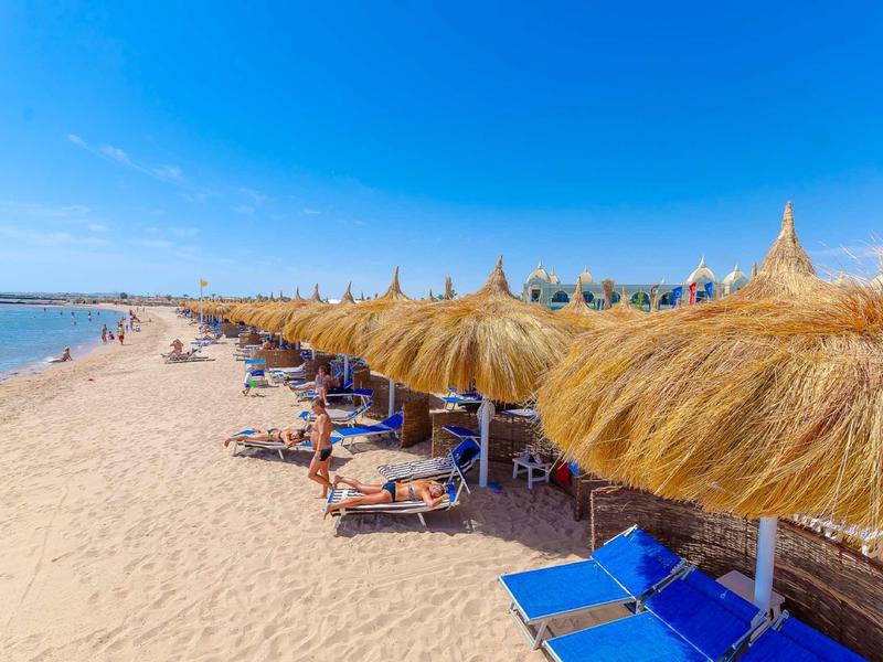 Plage de sable avec rangées de transats bleus et parasols en paille sous un ciel bleu clair