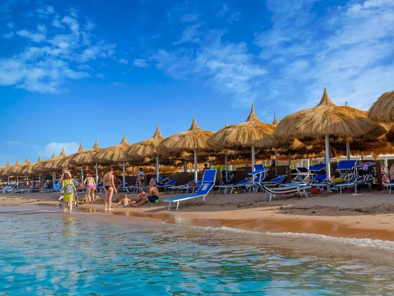 Plage avec de nombreux parasols en paille et chaises longues près de l'eau claire sous un ciel bleu