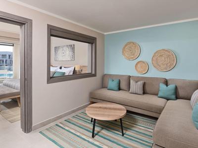 Helles Wohnzimmer mit Ecksofa, türkisen Wänden, rundem Holztisch und dekorativen Wandkörben.