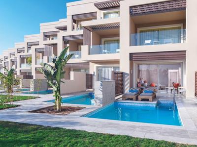 Moderne Reihenhäuser mit Terrassen, blauen Pools und grüner Rasenfläche unter klarem Himmel.