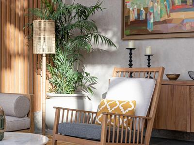 Helles Wohnzimmer mit Holzstuhl, großem Pflanzentopf, Teppich und farbenfrohem Gemälde.