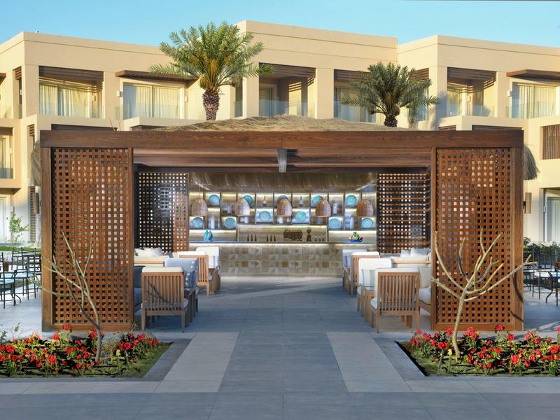 Moderner Außenbereich mit Holzbalken, dekorativen Pflanzen und Sitzgelegenheiten vor einem Gebäude.