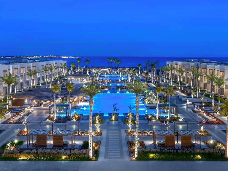 Symmetrischer Außenbereich mit beleuchteten Pools und Sitzbereichen zwischen zwei langen Gebäuden bei Nacht.