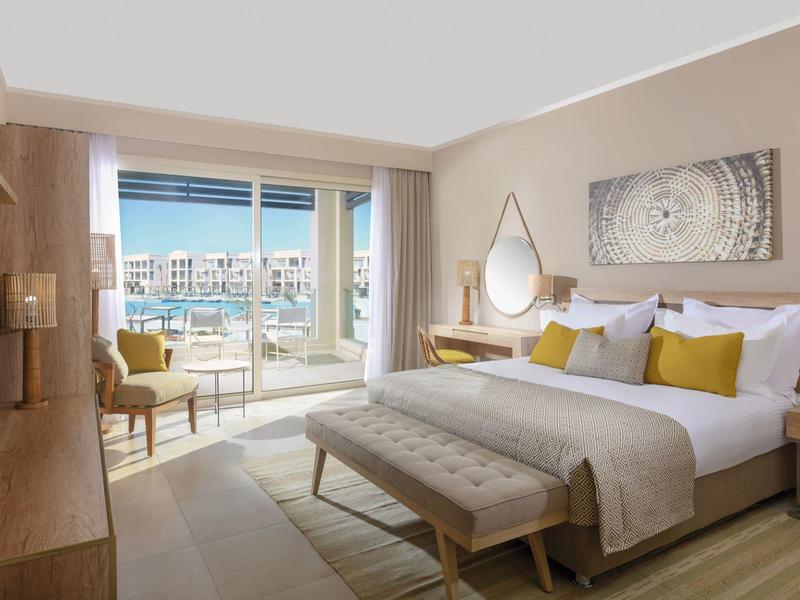 Helles Hotelzimmer mit Doppelbett, Balkon, Sesseln und moderner Holzmöblierung.