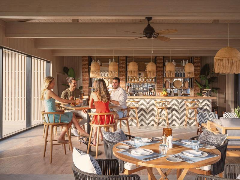 Modernes Restaurant mit Holzstühlen, Tischdeko und vier Personen im Gespräch in heller Atmosphäre.