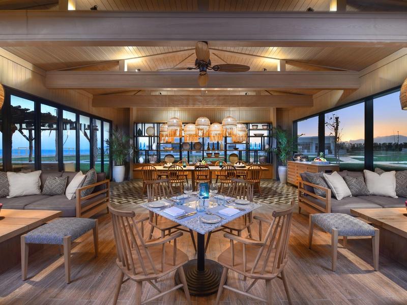 Modernes Restaurant mit Holzdecke, gemütlichen Sesseln und Blick auf das Meer bei Sonnenuntergang.