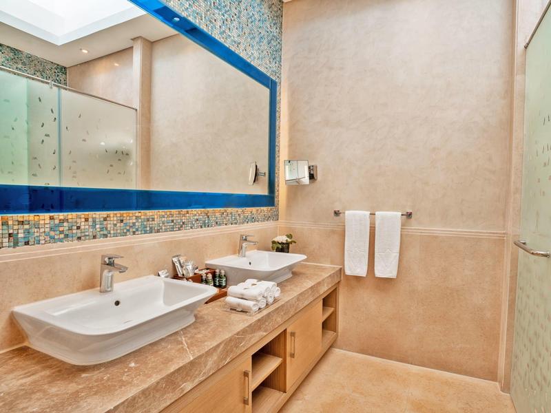 Modern, bright bathroom area with large mirror wall, two sinks, and beige wall covering.