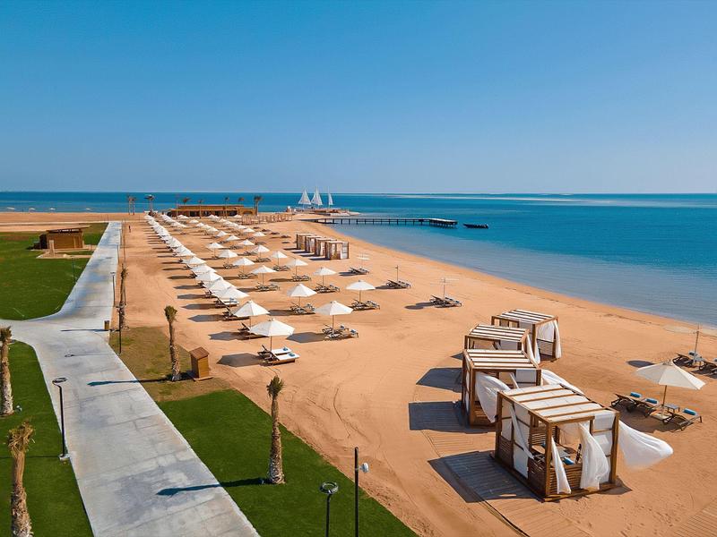 Wide beach with white umbrellas and beach chairs beside calm sea and blue sky.