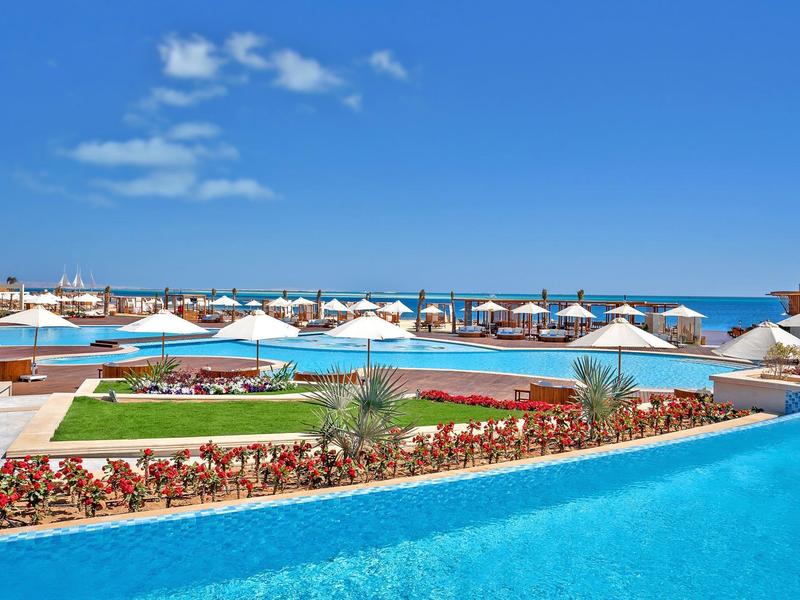 View of a hotel pool with sun umbrellas and flower beds by the sea.