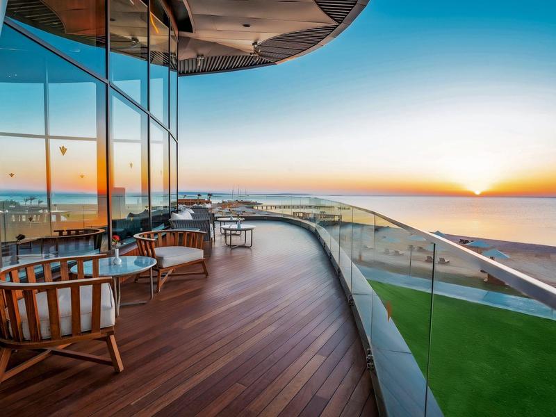Large balcony with wooden floor and seating overlooking the sea at sunset.