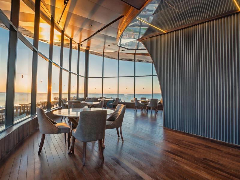 Modern hotel dining area with panoramic sunset views and comfortable chairs.