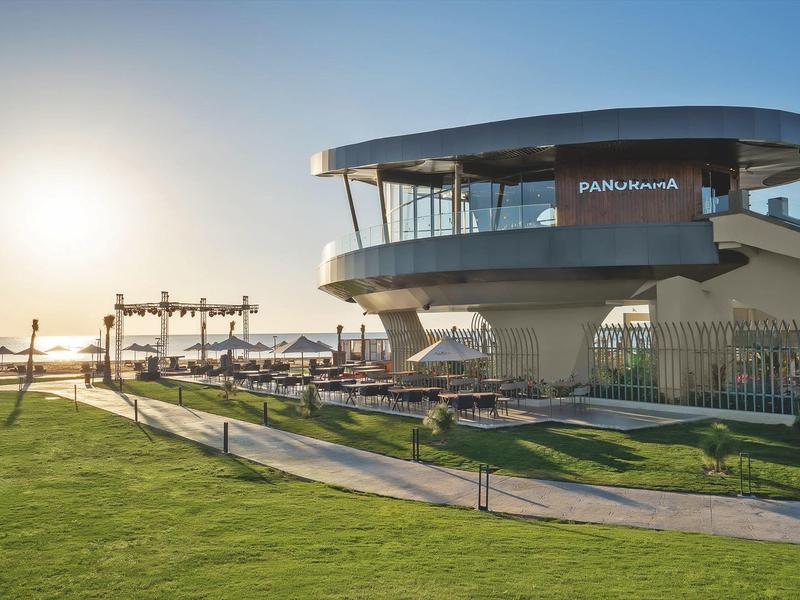 Modern circular building with glass facades next to a lawn at sunset.