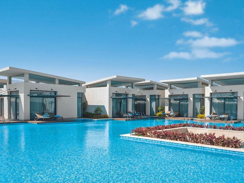 Modern bungalows with covered terraces by a large blue pool under a sunny sky.