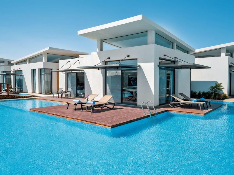 Modern white villas with large glass windows and terraces by the blue pool.