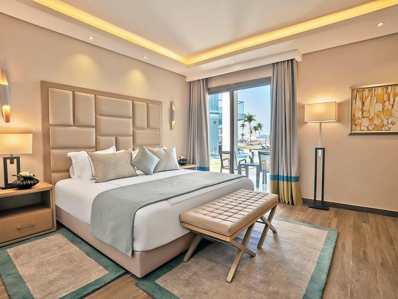 Modern hotel room with large bed, soft pillows, wooden floor, and balcony overlooking the sea