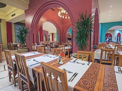 Restaurant mit Holzstühlen, weißen Tischdecken und warmen roten Wänden, dekoriert mit Pflanzen.