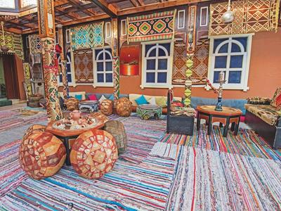 Buntes Café mit gemusterten Sitzkissen, Holztischen, Teppichen und verzierter Wanddekoration.
