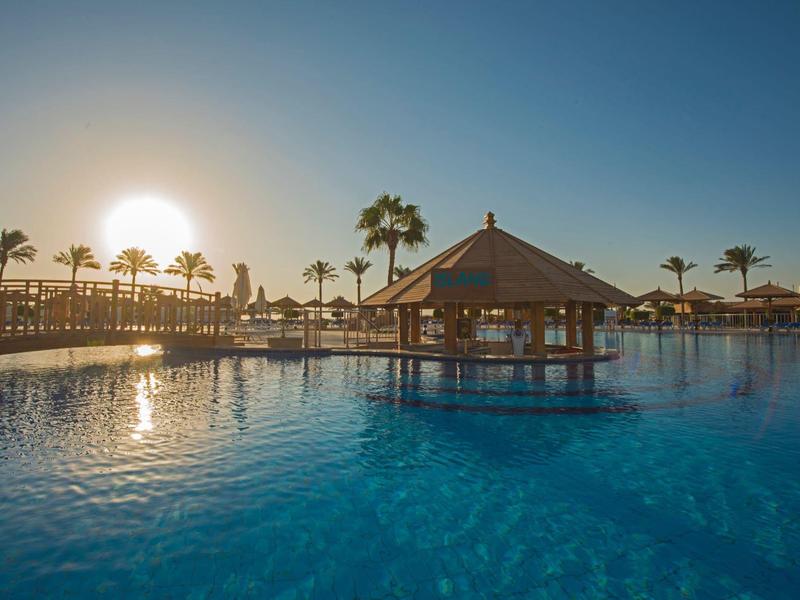 Velký hotelový bazén s pavilonem uprostřed a palmami při západu slunce