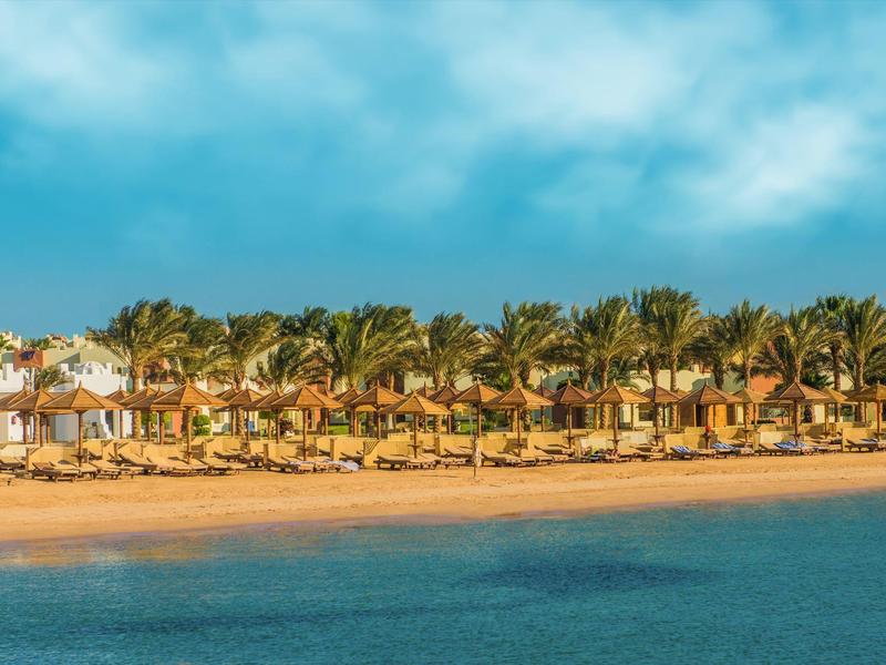 Plážový hotel s palmami a lehátky u klidného modrého moře pod modrou oblohou