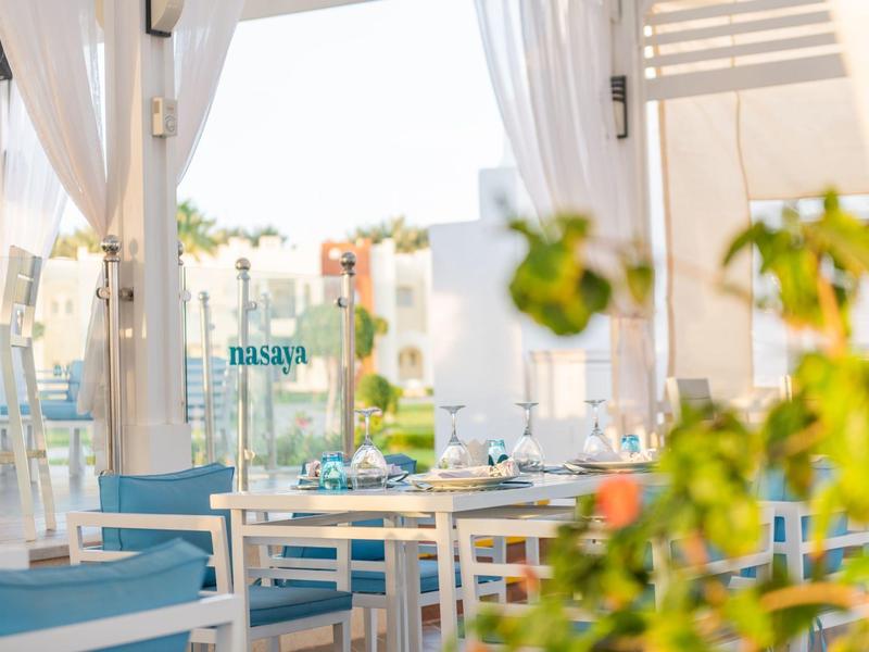 Moderní, vzdušná restaurace s bílým nábytkem a modrým dekorem, výhled na palmy.