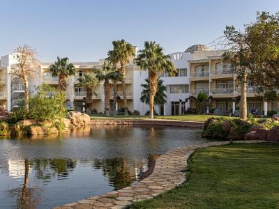 Edificio del hotel con balcones junto a un estanque y palmeras al atardecer