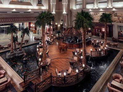 Interior de hotel lujoso con fuentes, palmeras y un elegante puente de madera.
