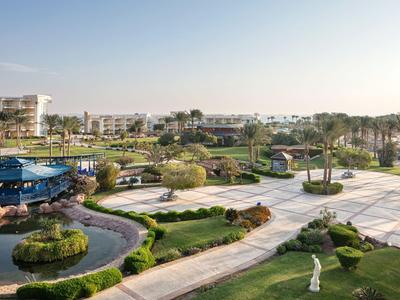 Gran jardín del hotel con senderos, áreas verdes, palmeras y edificios cercanos bajo cielo despejado.