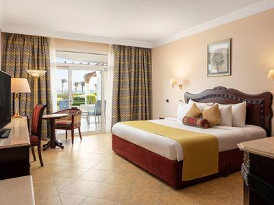 Pohodlný hotelový pokoj s velkou postelí, televizí, psacím stolem a balkonovými dveřmi.