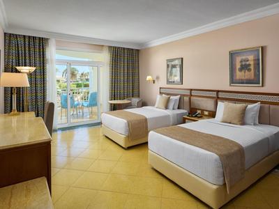 Hotelový pokoj se dvěma postelemi, balkonem a výhledem na palmy.