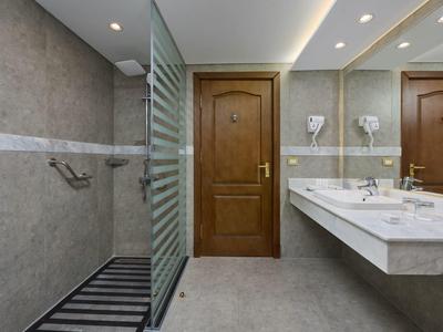 Moderní hotelová koupelna se dřevěnými dveřmi, skleněnou přepážkou sprchy a dvojitým umyvadlem.