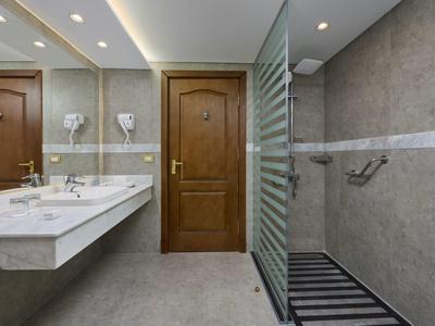 Moderní koupelna s mramorovým umyvadlem, dřevěnými dveřmi a dlaždičkovou sprchou se skleněnou příčkou.