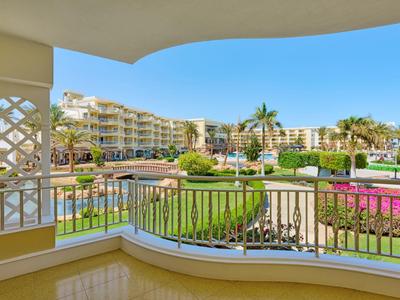 Výhled z balkonu na bazén, zahrady a budovy resortu pod jasnou oblohou.