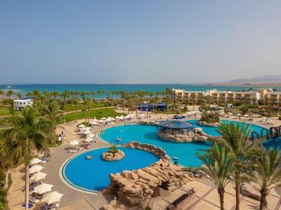 Bazénová oblast resortu s palmami, lehátky a výhledem na oceán za slunečného dne.