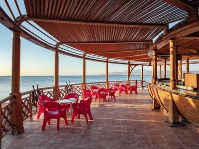 Terraza cubierta con sillas rojas y bar con vista al mar al atardecer.