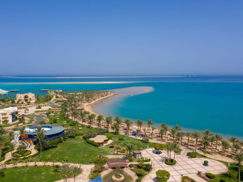 Pobřežní resort s palmami, písečnou pláží a tyrkysovým mořem pod jasně modrou oblohou.