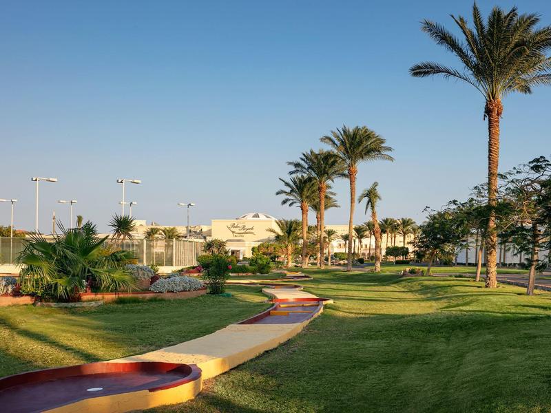 Kvetoucí zahrada s palmami a cestou pod jasnou modrou oblohou v letovisku.