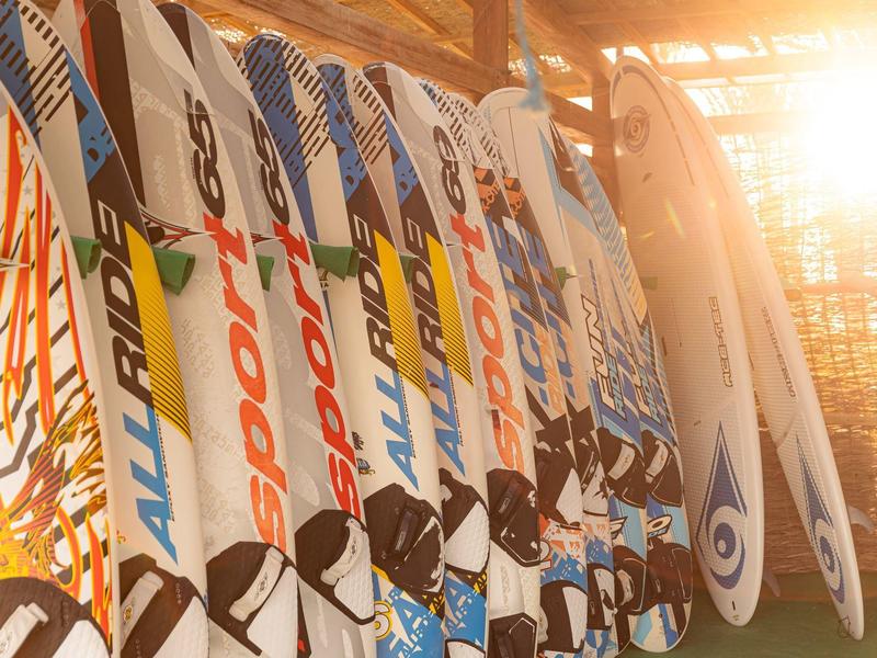 Slunečně osvětlená řada barevných windsurfových prken uvnitř.