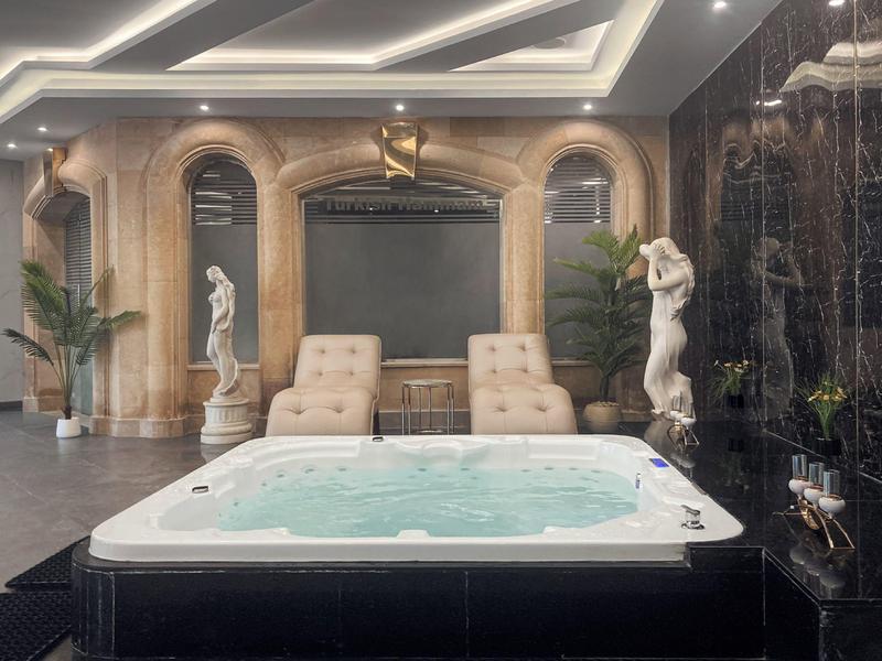 Vnitřní spa s jacuzzi, klasickými sochami, lehátky a dekorativními oblouky.